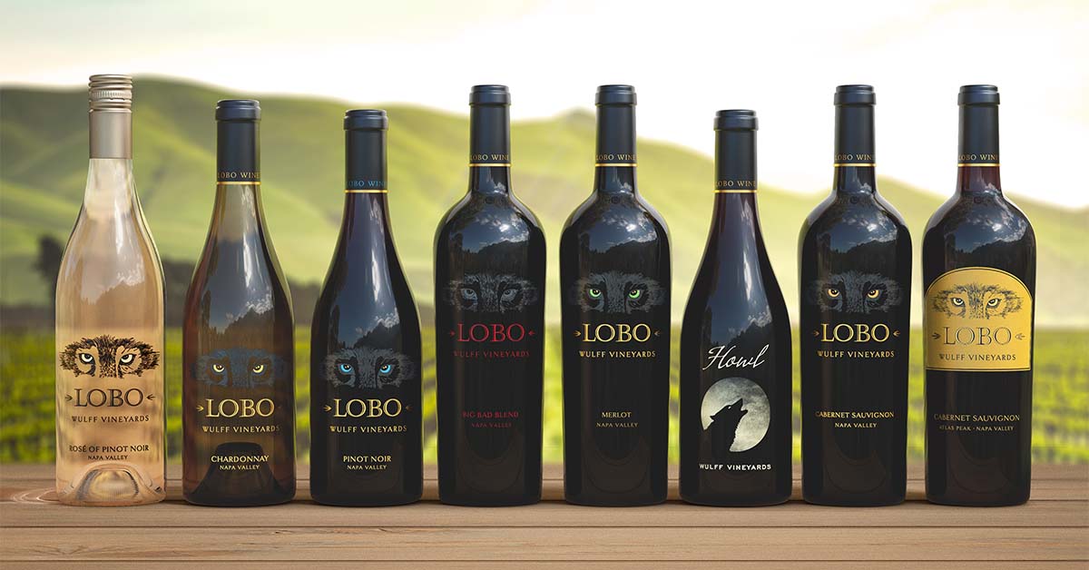 lineup of wine bottles of different shapes and sizes on a wood table in front of a green landscape