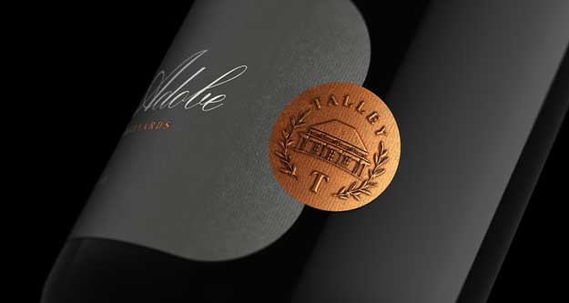 The Adobe by Talley Vineyards bottle close-up, copper embossed estate crest on a grey textured label, by Outshinery