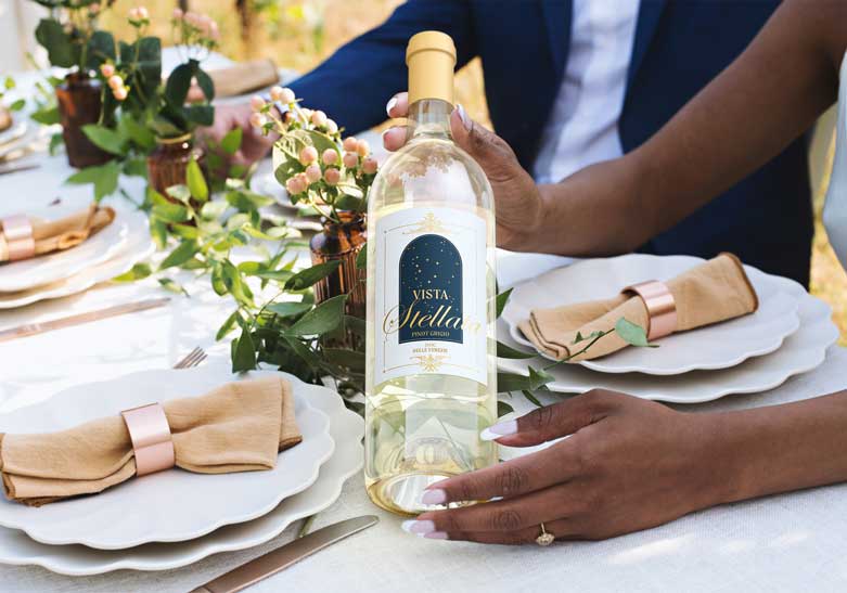 Vista Stellata Pinot Grigio bottle on an outdoor wedding table with scalloped plates and copper napkin rings, by Outshinery