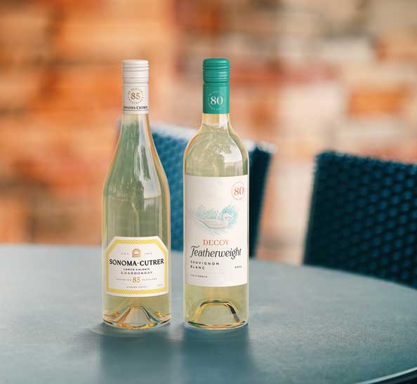 Sonoma-Cutrer Lower Calorie Chardonnay and Decoy Featherweight Sauvignon Blanc on a patio table, by Outshinery