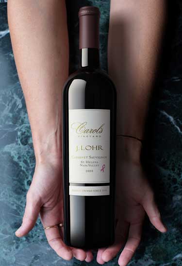 J. Lohr Carol's Vineyard 2023 St. Helena Cabernet Sauvignon bottle held in two hands over green marble, by Outshinery