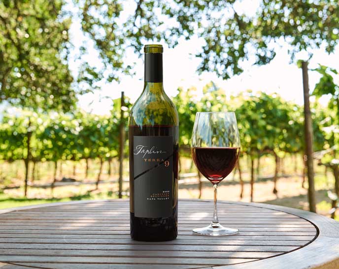Taplin Terra 9 2023 Napa Valley Cabernet Sauvignon bottle and poured glass on a table in the vineyard, by Outshinery