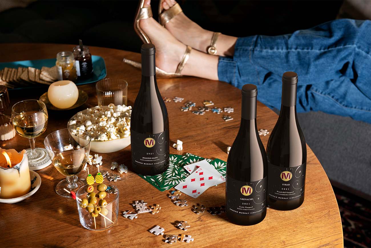 Andrew Murray Vineyards Roasted Slope, Grenache, and Syrah 2021 bottles in a game-night lifestyle scene rendered by Outshinery Studio