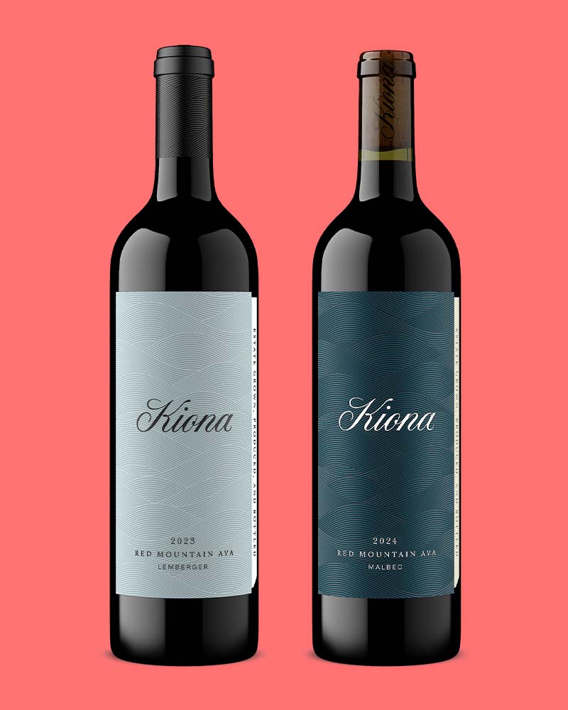 Two Kiona Red Mountain AVA wine bottles, a 2023 Lemberger and 2024 Malbec, with foil-topped closures on a coral background