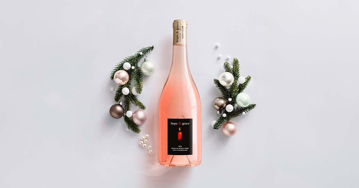 Hope & Grace Rosé of Pinot Noir bottle shot in gold foil, styled with holiday pine wreaths, pearls, and ornaments for a winter gift campaign