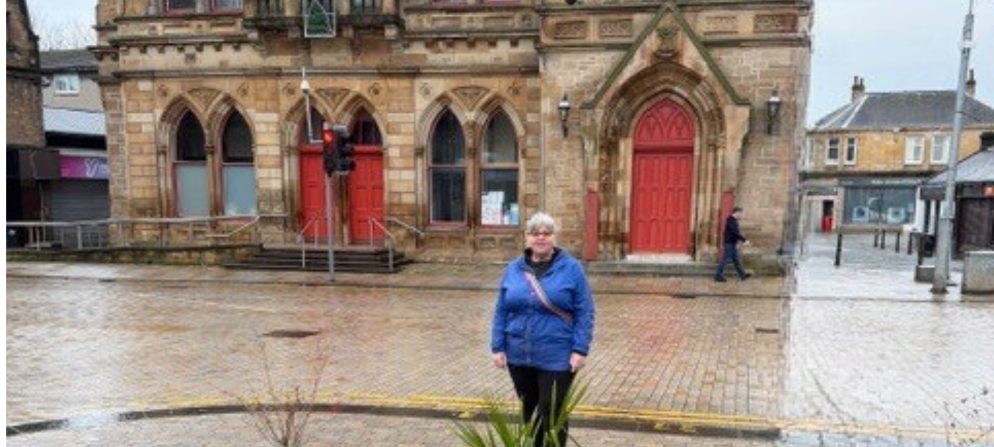 A woman stands in a town square, with a historic-looking building behind her.