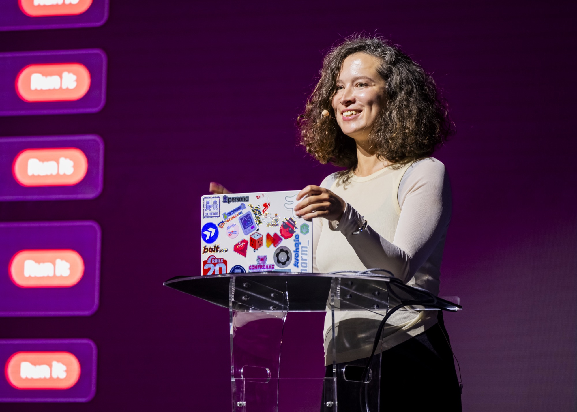 Irina Nazarova at the podium at Agent Night, holding up a sticker-covered laptop.