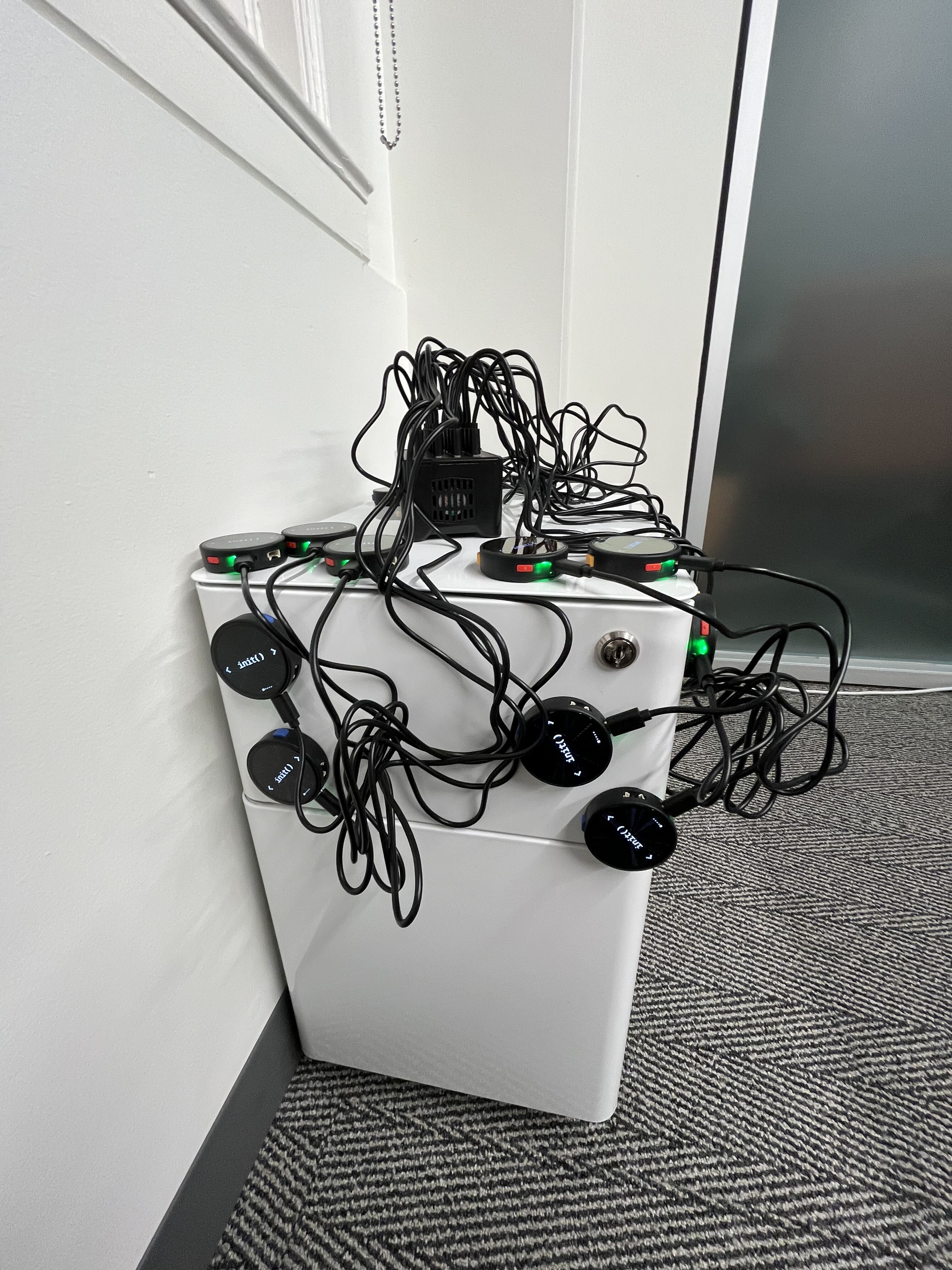Round init() badges stuck to a white filing cabinet and connected to a tangle of USB charging cables.