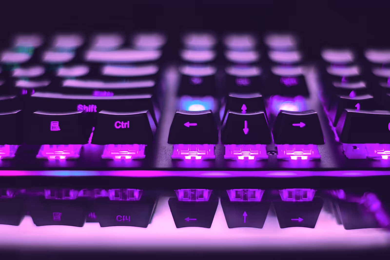 A purple LED computer keyboard glows in a dark room