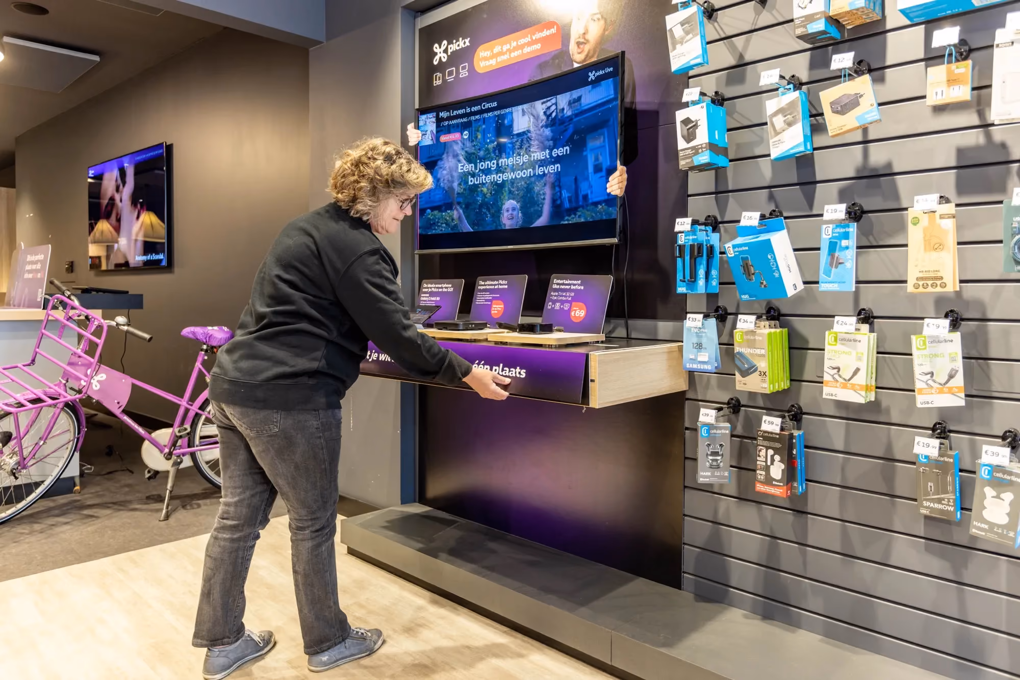 Proximus store accessories wall with mobile device cases, chargers, and a cargo bike nearby