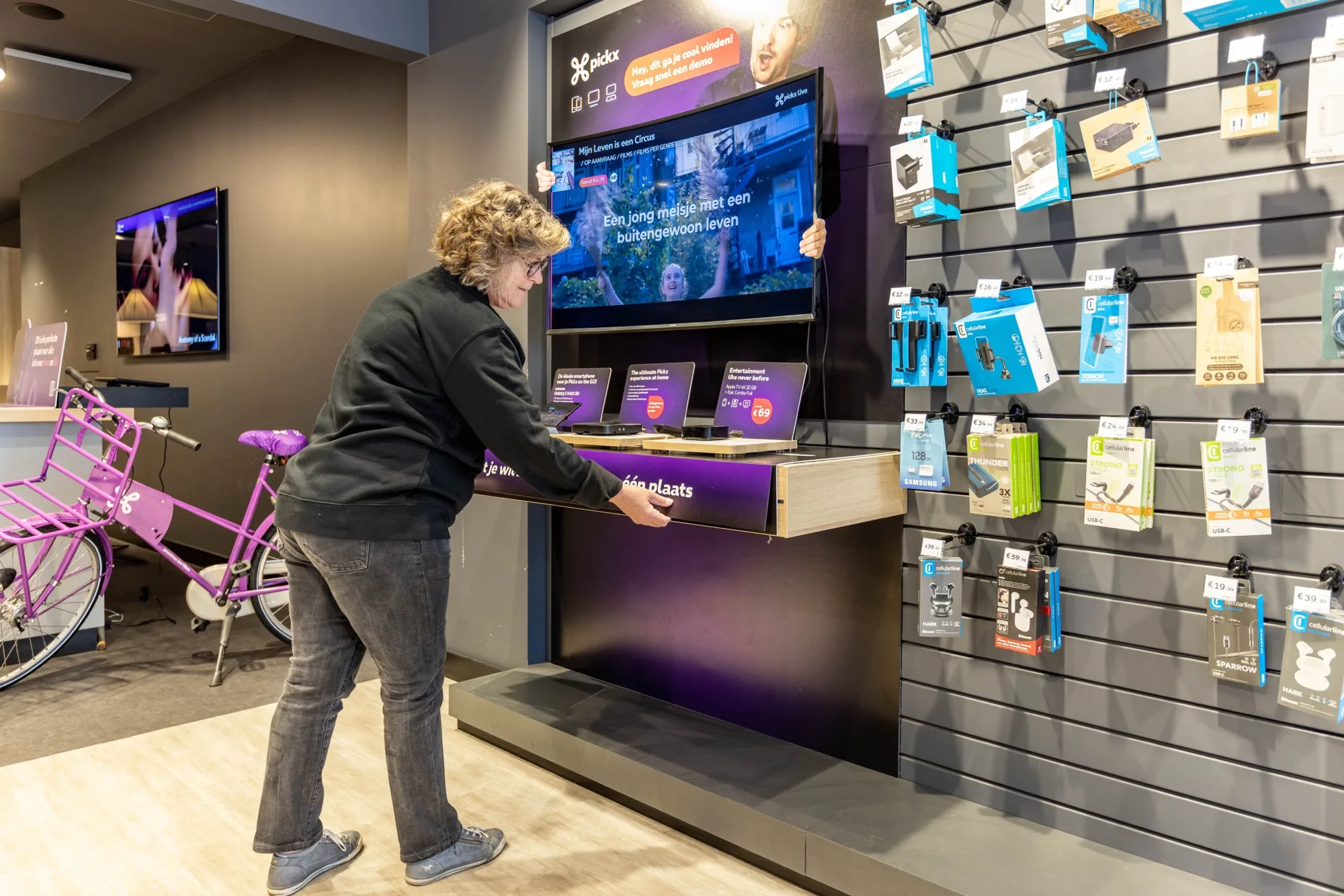 Proximus store accessories wall with mobile device cases, chargers, and a cargo bike nearby
