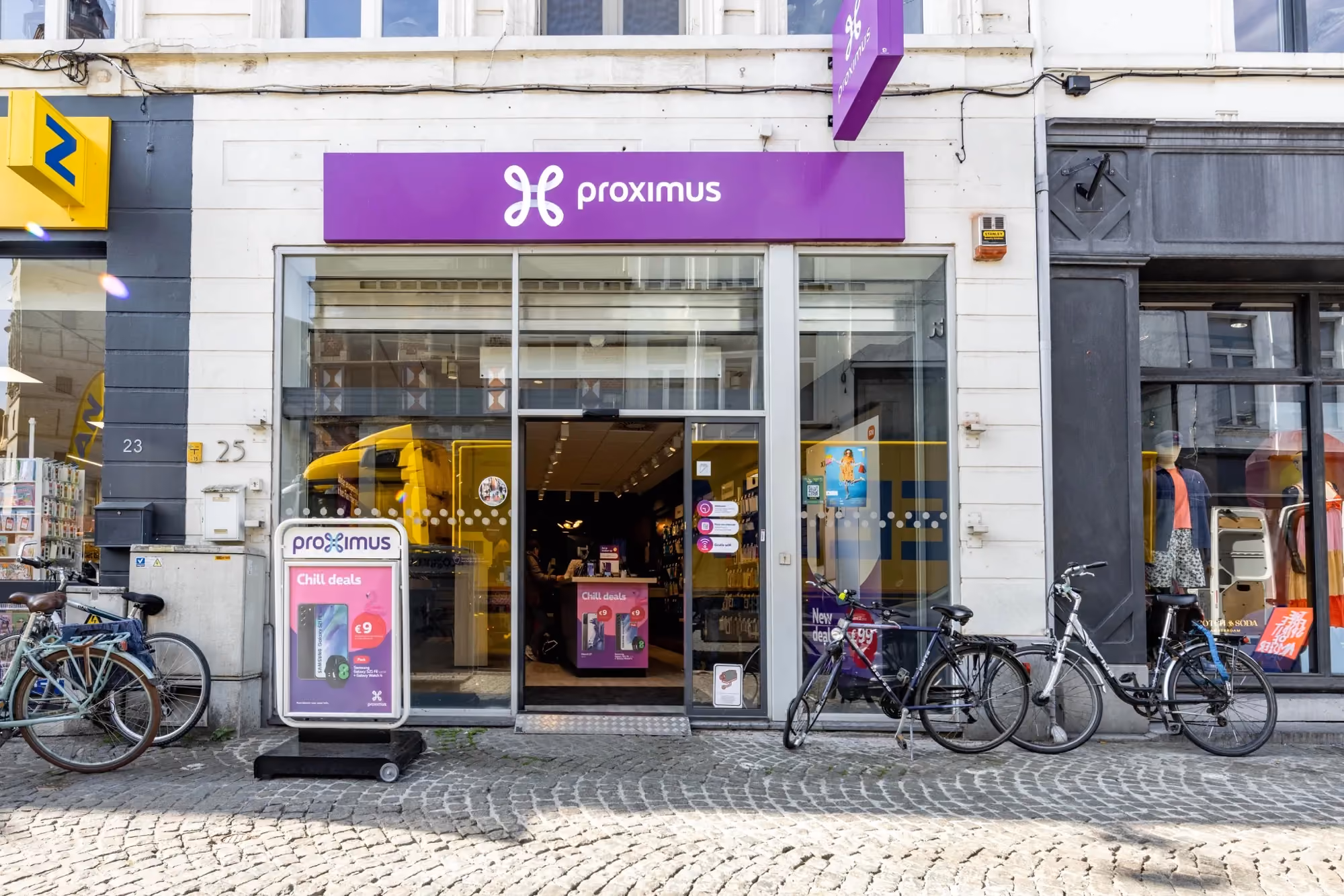 Exterior storefront of a Proximus shop with window displays and parked bicycles