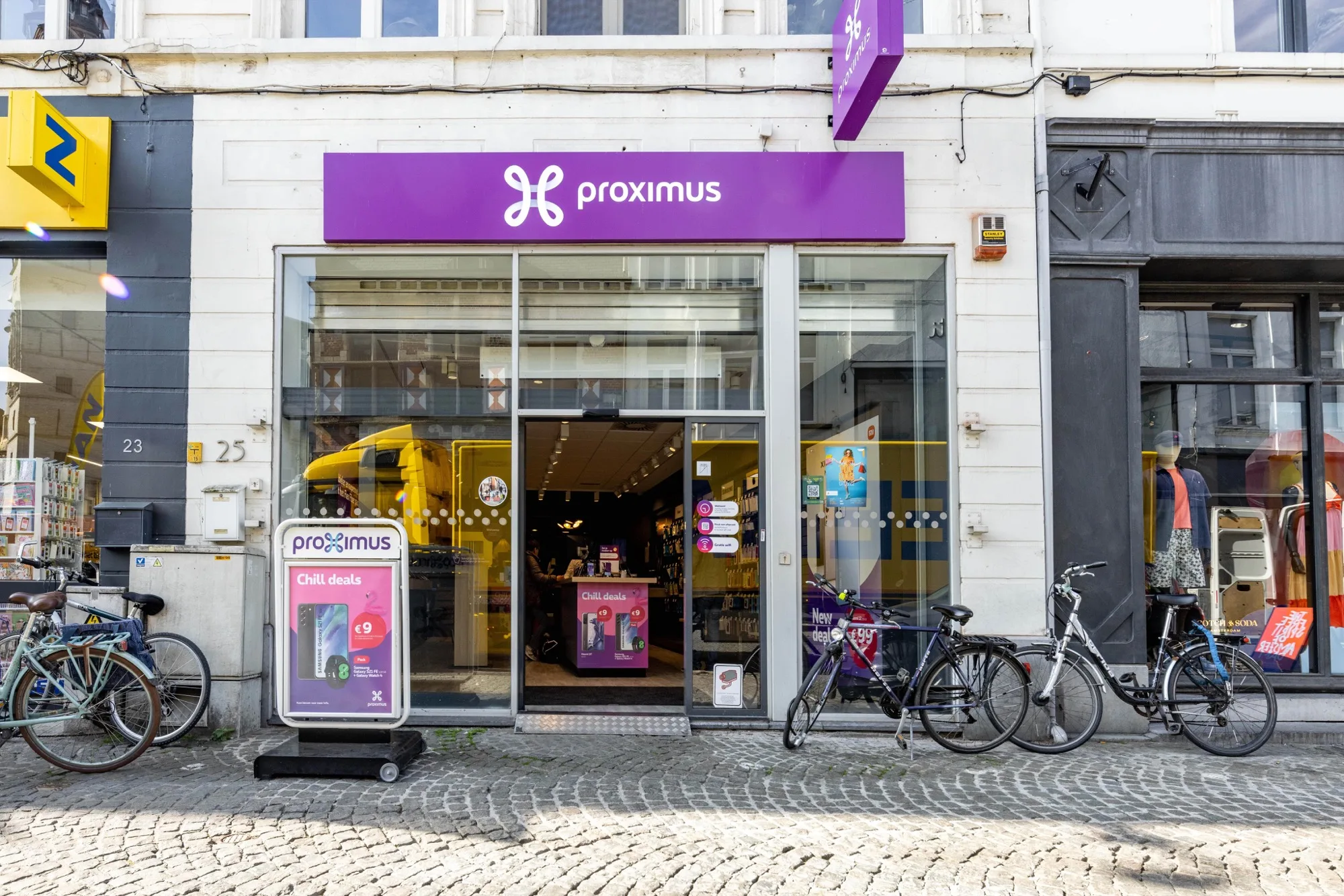 Exterior storefront of a Proximus shop with window displays and parked bicycles