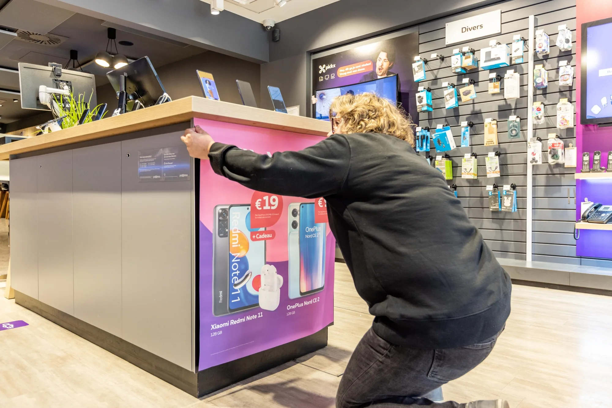 Field & Concept merchandiser installing a Xiaomi Redmi Note 11 and OnePlus Nord promotional display at a Proximus counter