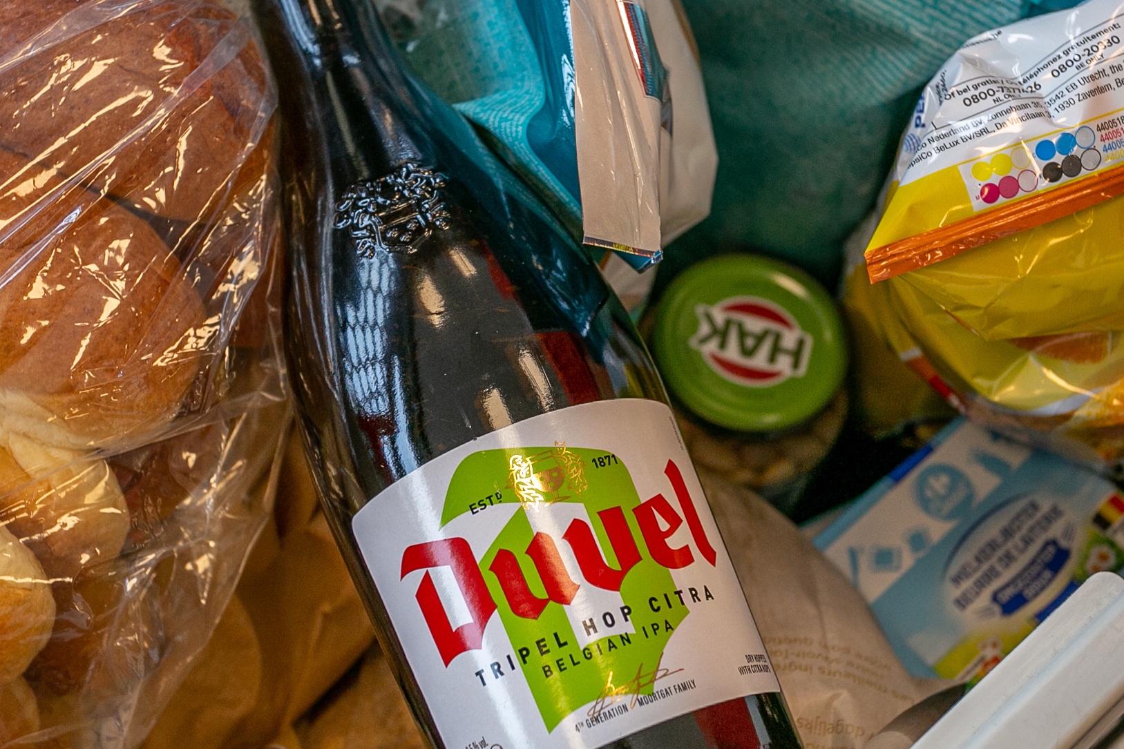 Bottle of Duvel Tripel Hop Citra Belgian IPA in a grocery shopping bag alongside bread and other purchases