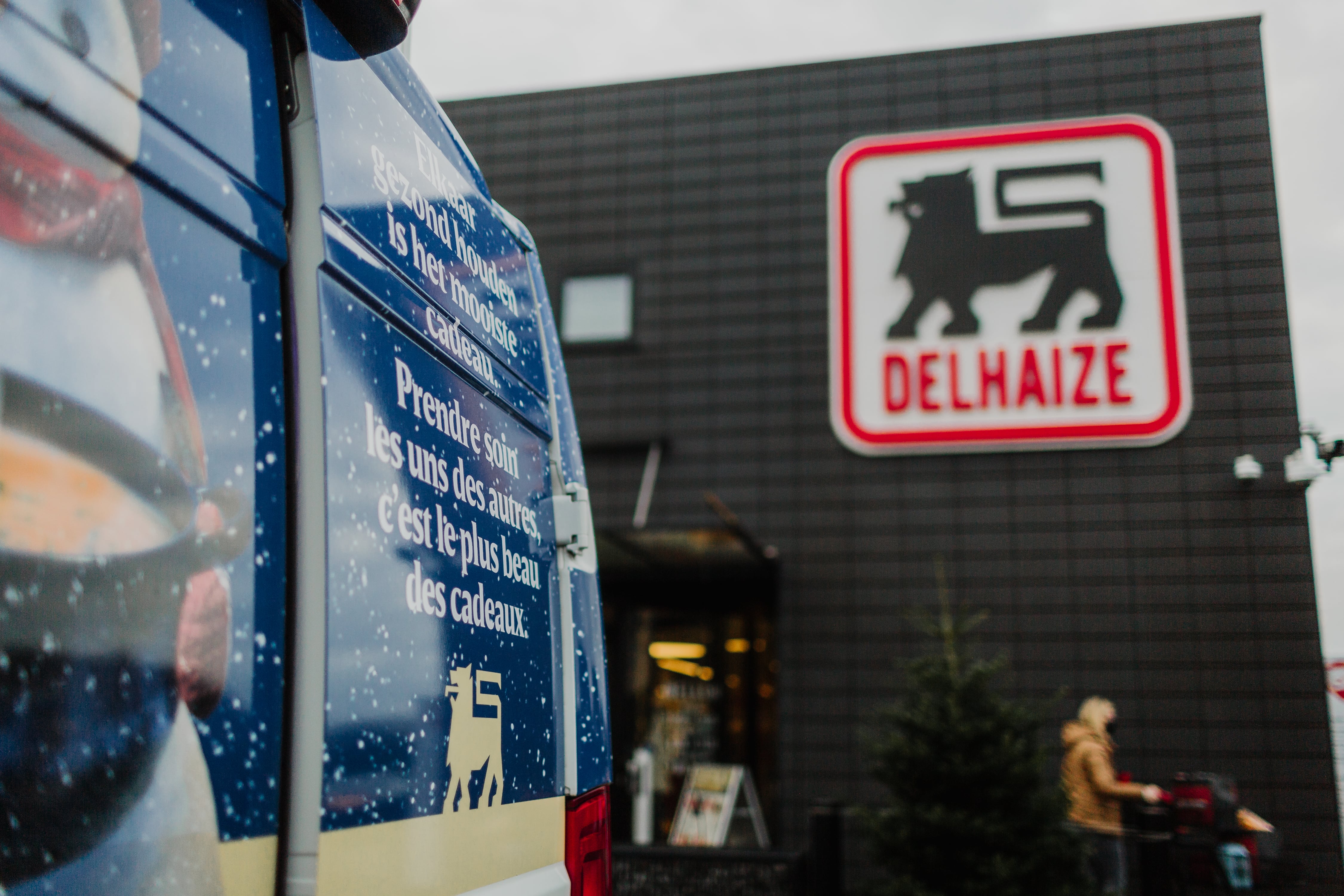 Delhaize storefront sign beside a branded delivery van with a holiday season message, part of a Field & Concept in-store activation