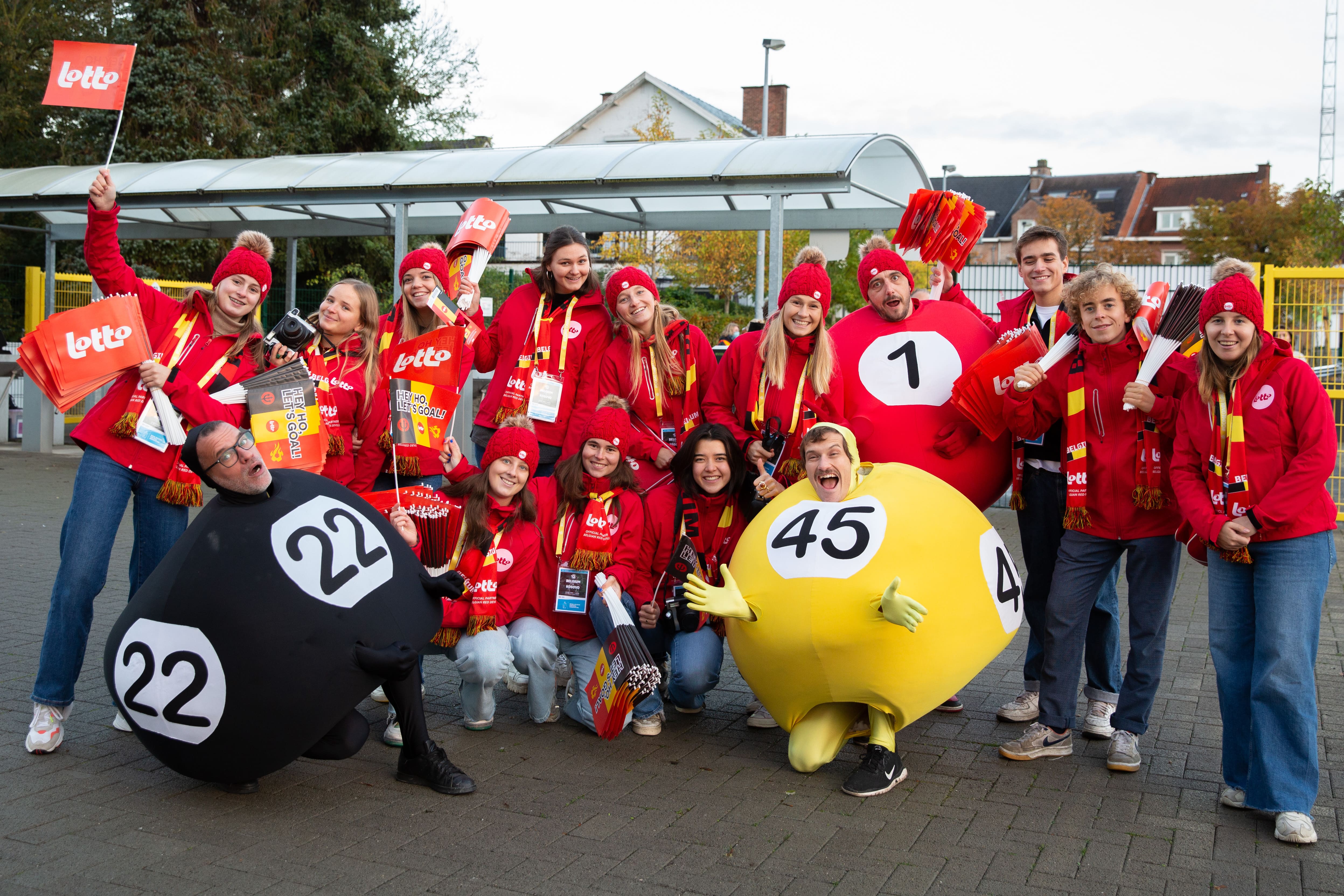 Field & Concept brand ambassador team in red Belgian National Lottery Lotto jackets posing with giant lottery ball costumes at an outdoor event