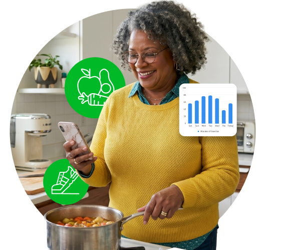 Smiling woman cooking soup while checking a health app on her phone in a bright kitchen.