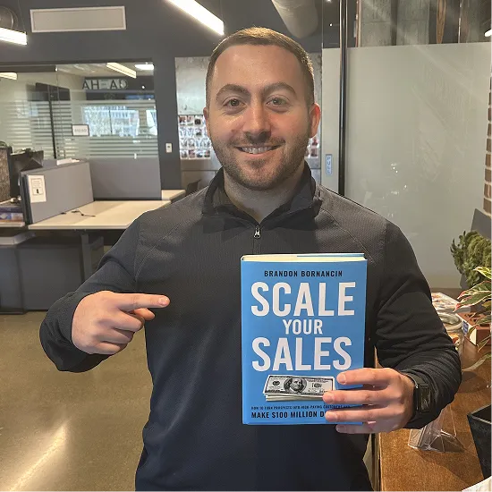 Man holding up and pointing to Scale Your Sales by Brandon Bornancin.