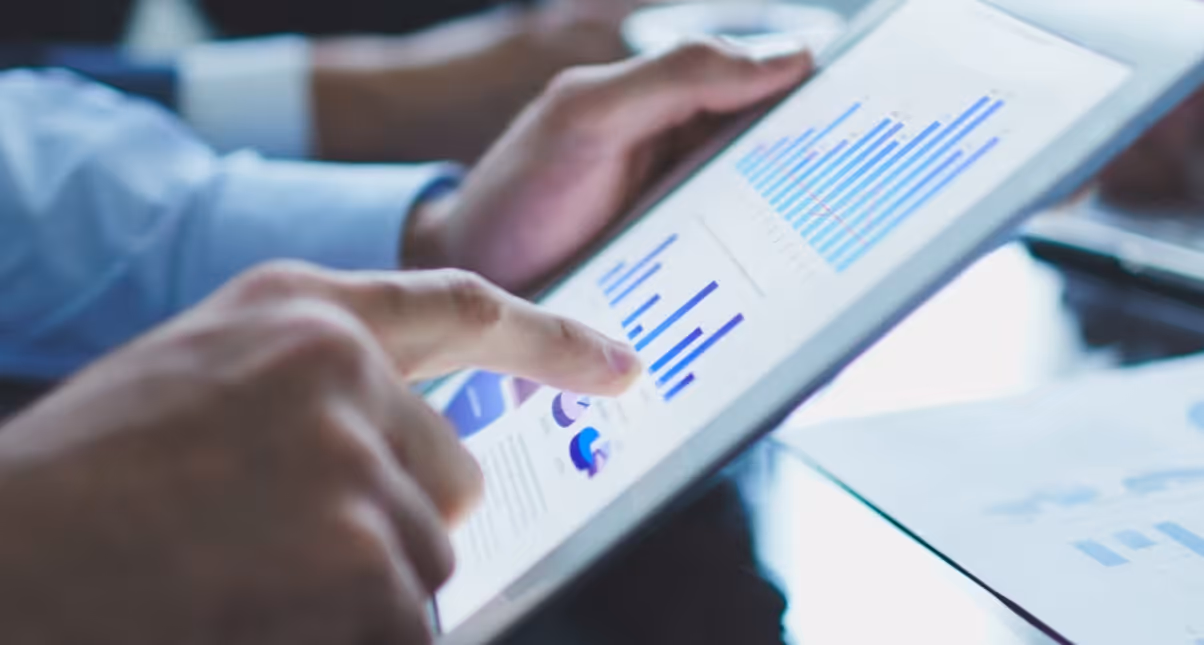 Person using a tablet displaying blue bar and pie charts with financial data.
