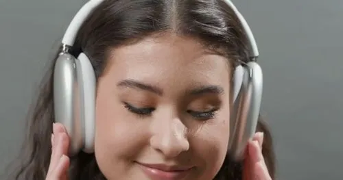A close-up of a person wearing over-ear headphones, smiling as they adjust them.