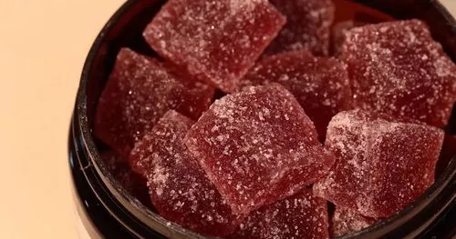 A close-up of a jar filled with sugar-coated gummies on a light background.