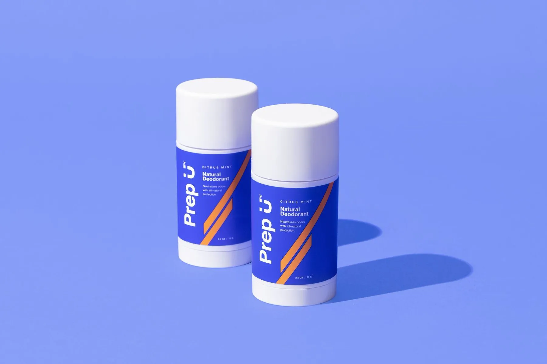 Two deodorant sticks on a pastel purple backdrop with long studio shadows