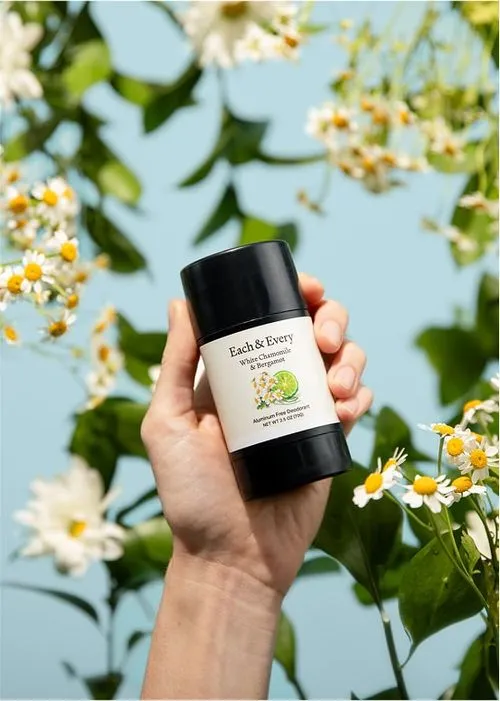 Hand holding Each & Every deodorant among white flowers