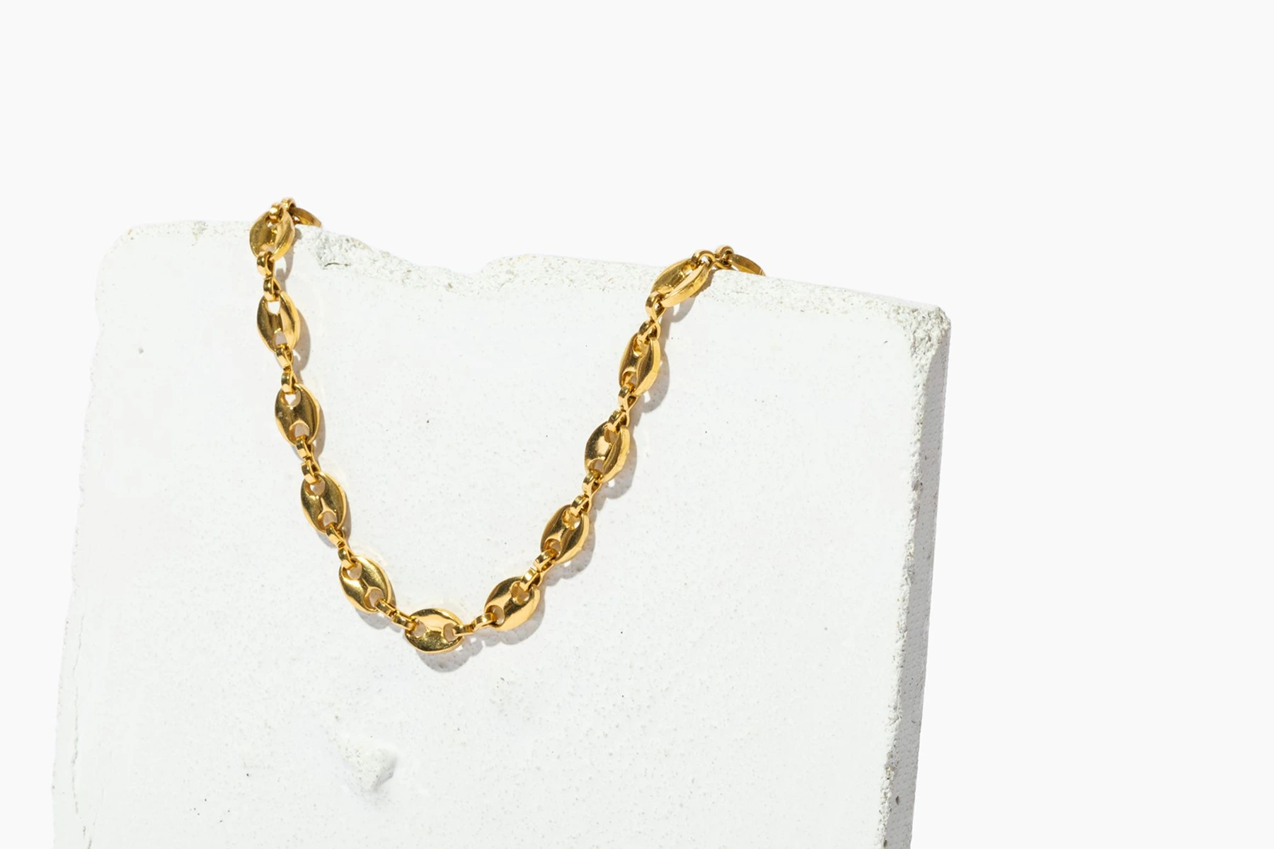 a gold necklace draped over a chalky stone