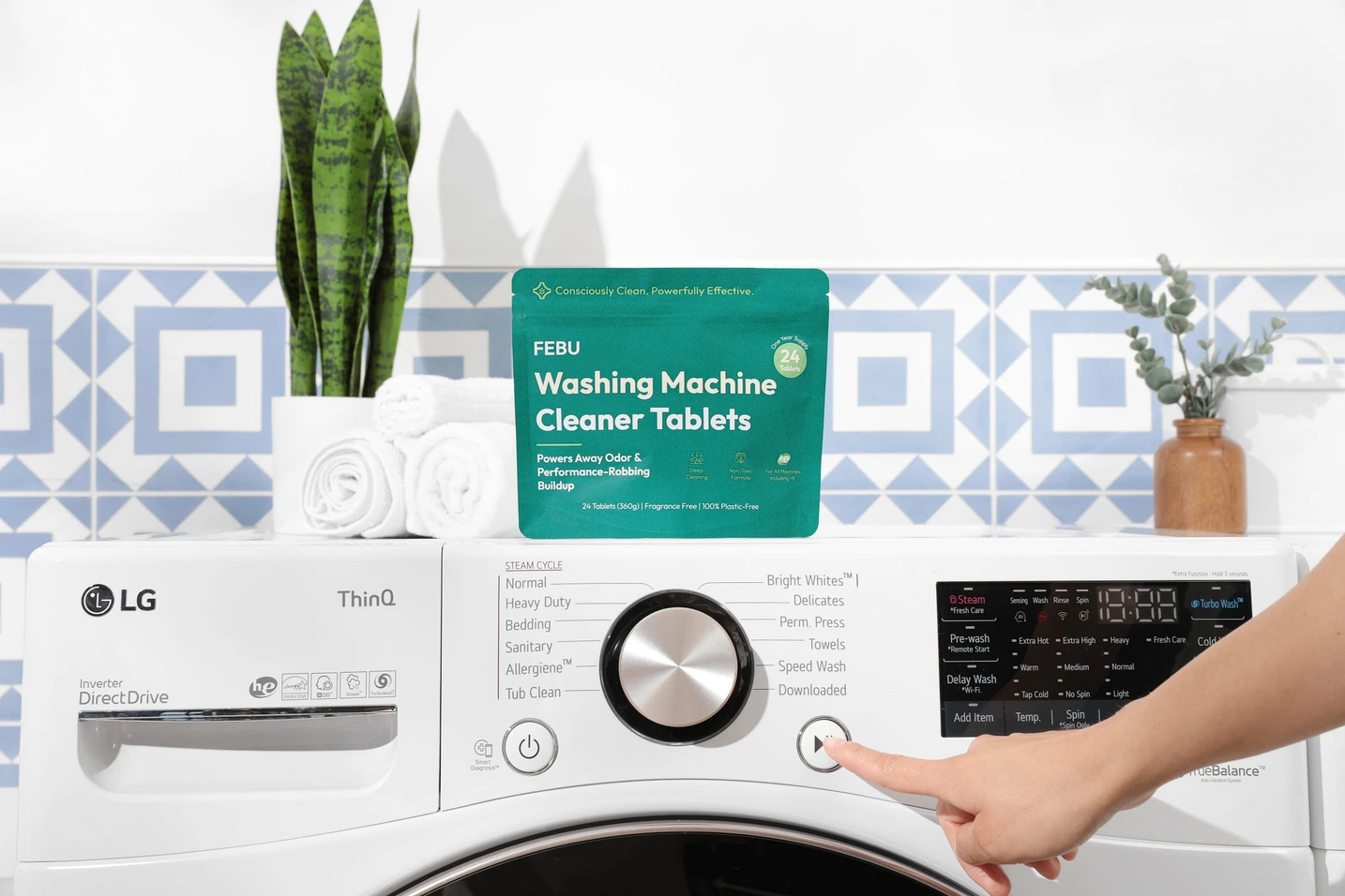hand pressings start button on a washing machine with cleaning tablets sitting on top.