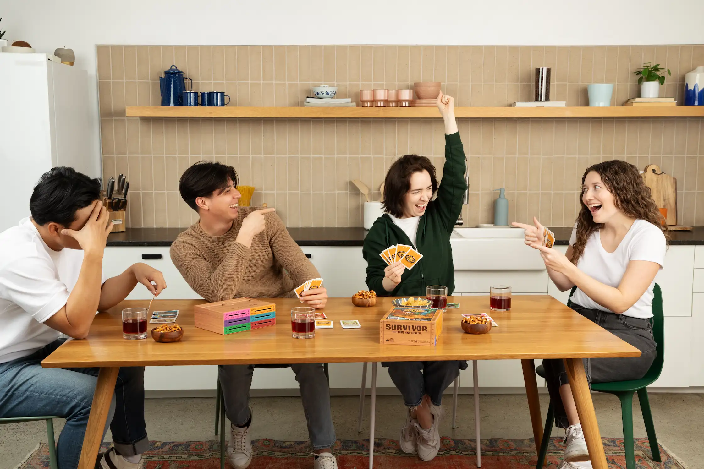 4 young adults playing a card game at a dining table in a kitchen