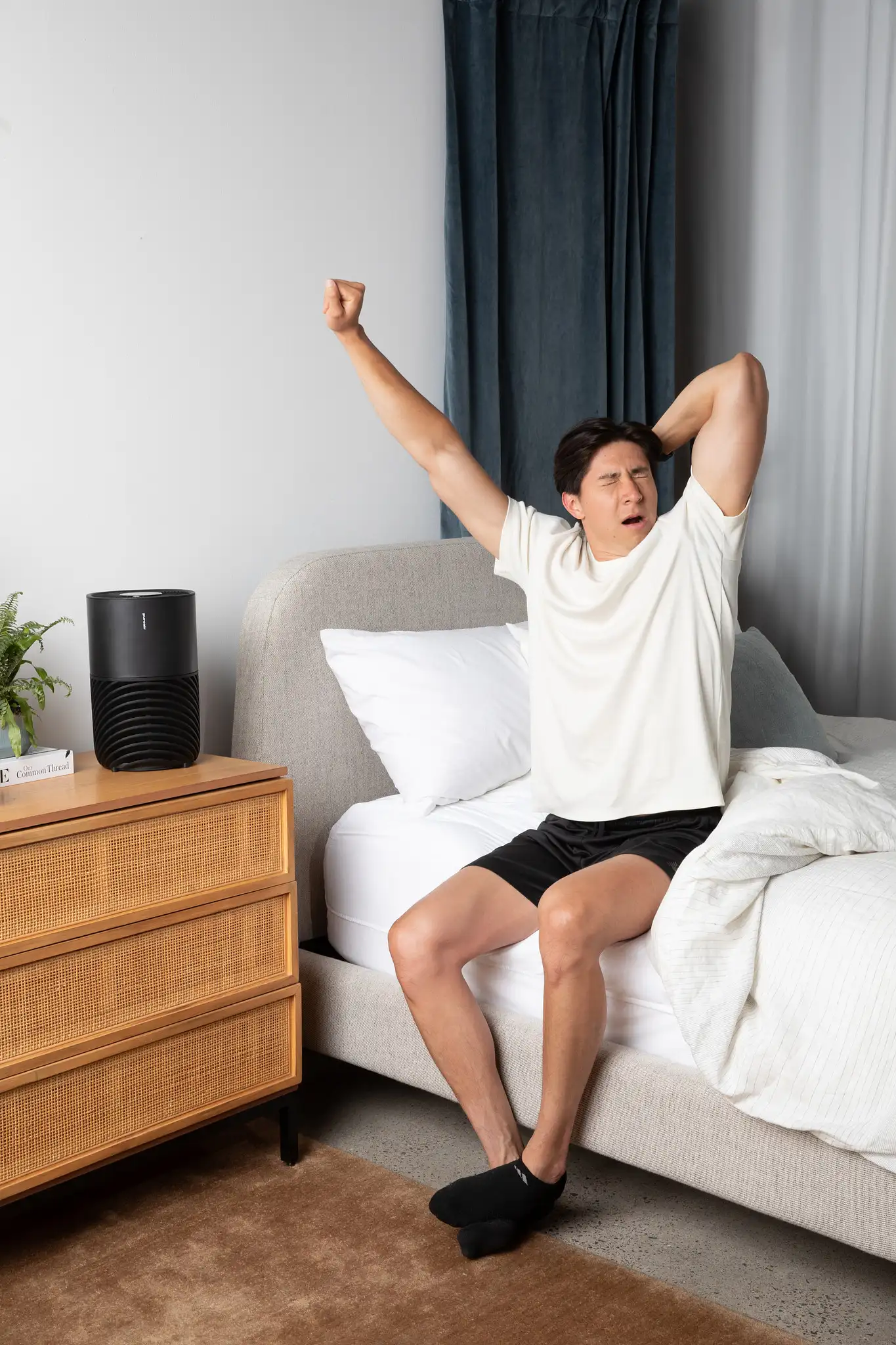 Man yawning on the side of a bed next to an air purifier