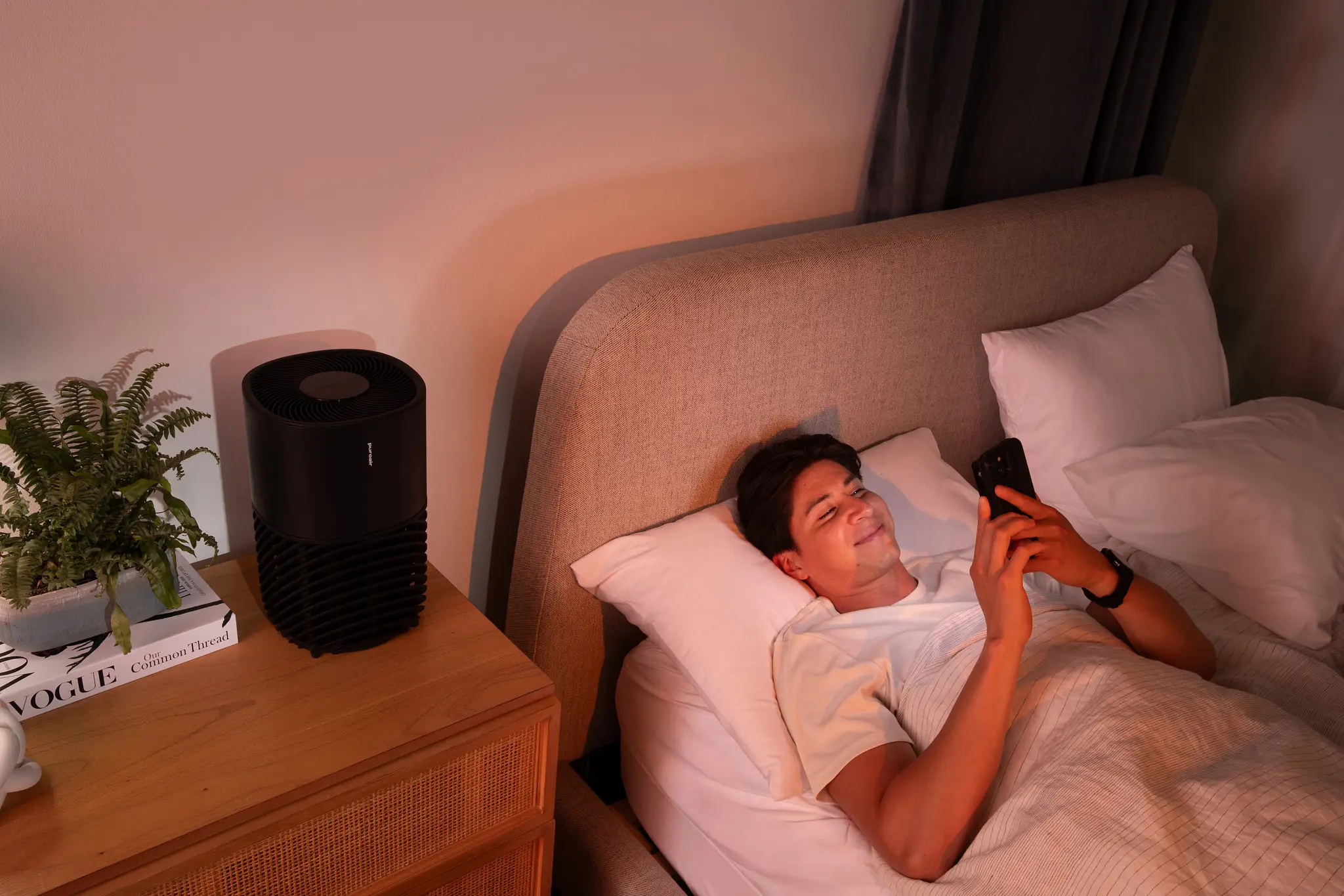 Man in bed on phone smiling next to air purifier