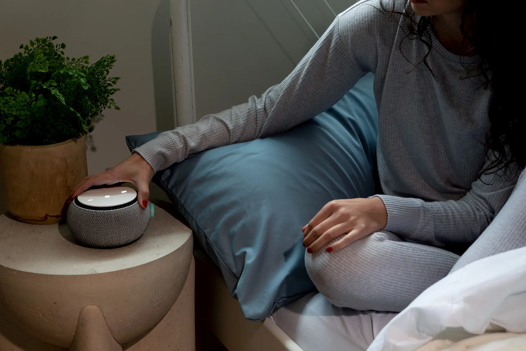 woman reaching for white noise machine on nightstand