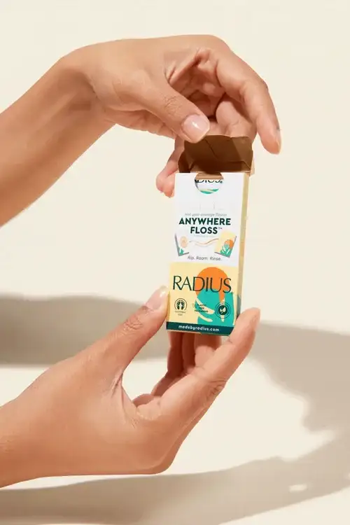 Hands holding an open box of Radius Anywhere Floss with visible product branding.