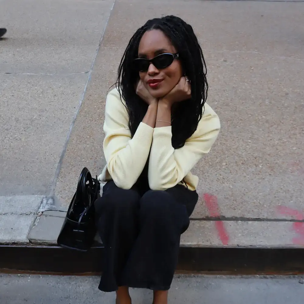 UGC creator sits on curb with cute outfit and sunglasses on, smiling at camera