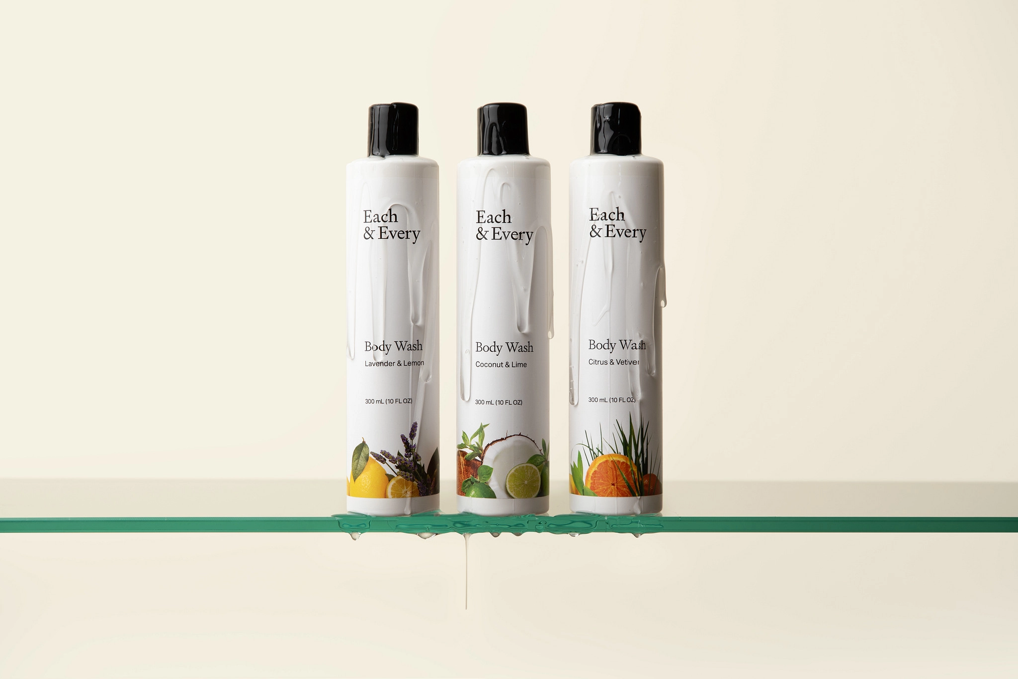 Three white Each & Every body wash bottles on a glass shelf with water dripping off the shelf edges.