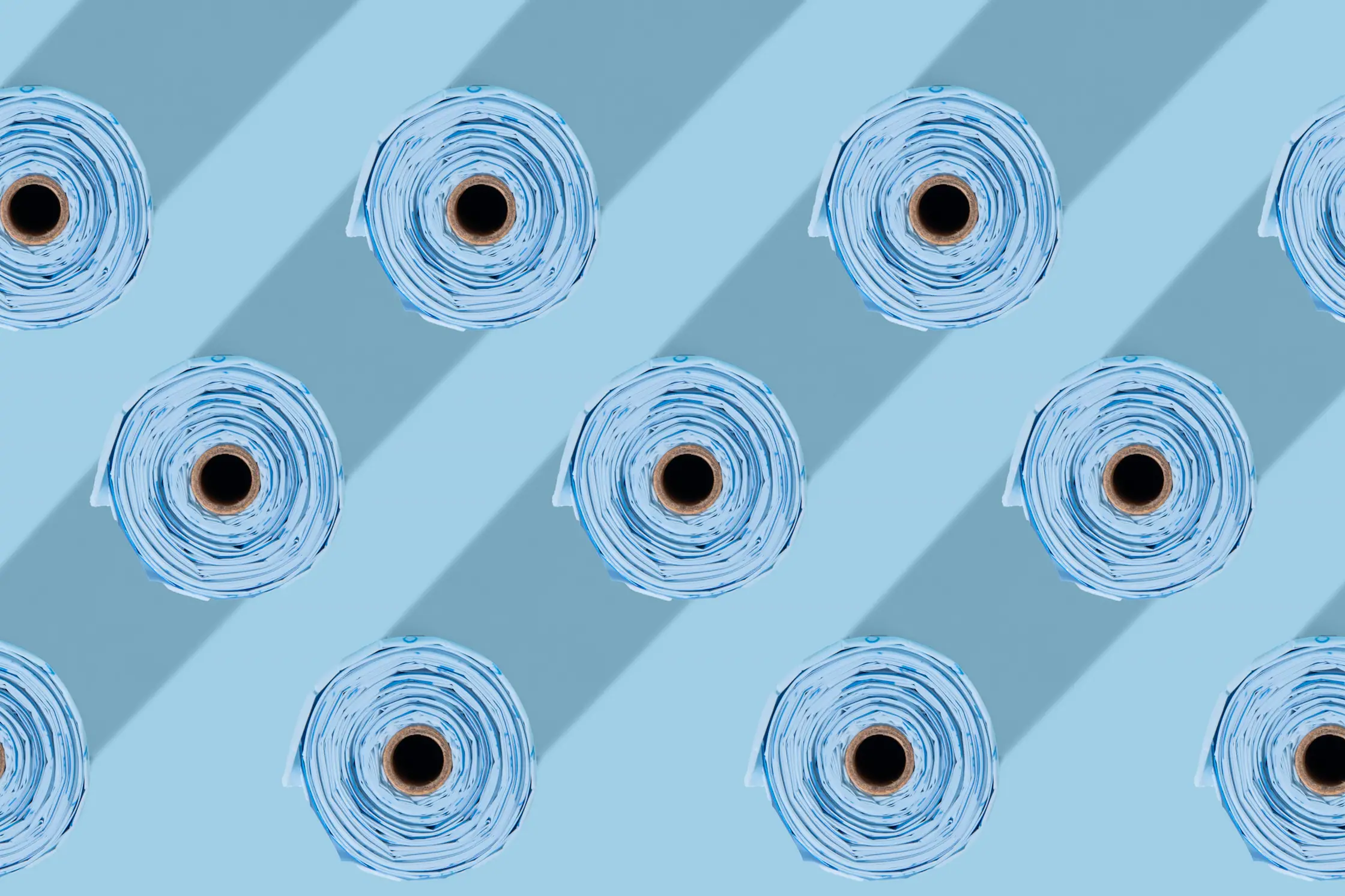 Top view of neatly arranged rolls of blue plastic bags casting diagonal shadows on a blue surface.