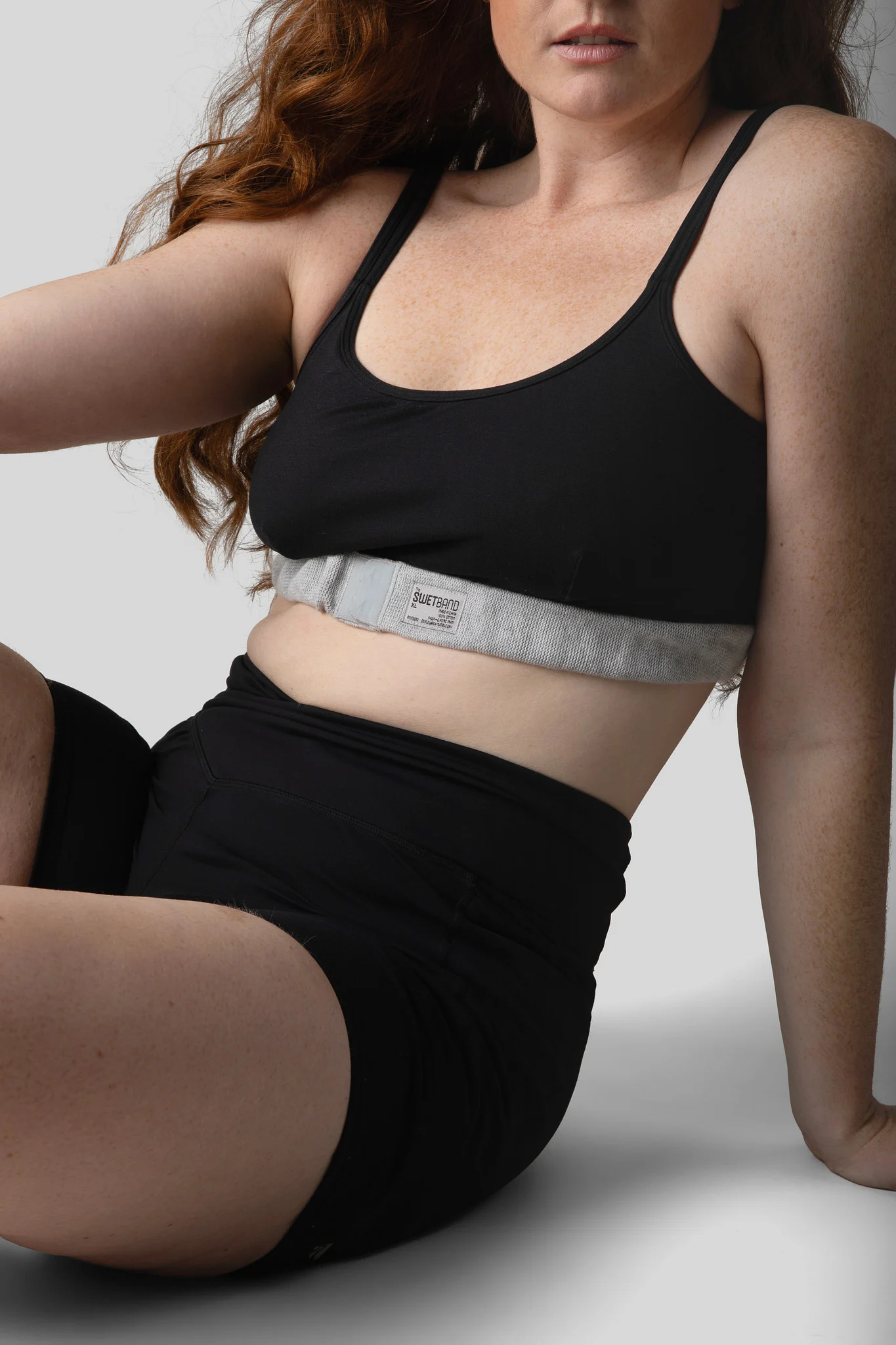 Partial view of a woman in black workout top and shorts sitting on the floor with wavy hair.