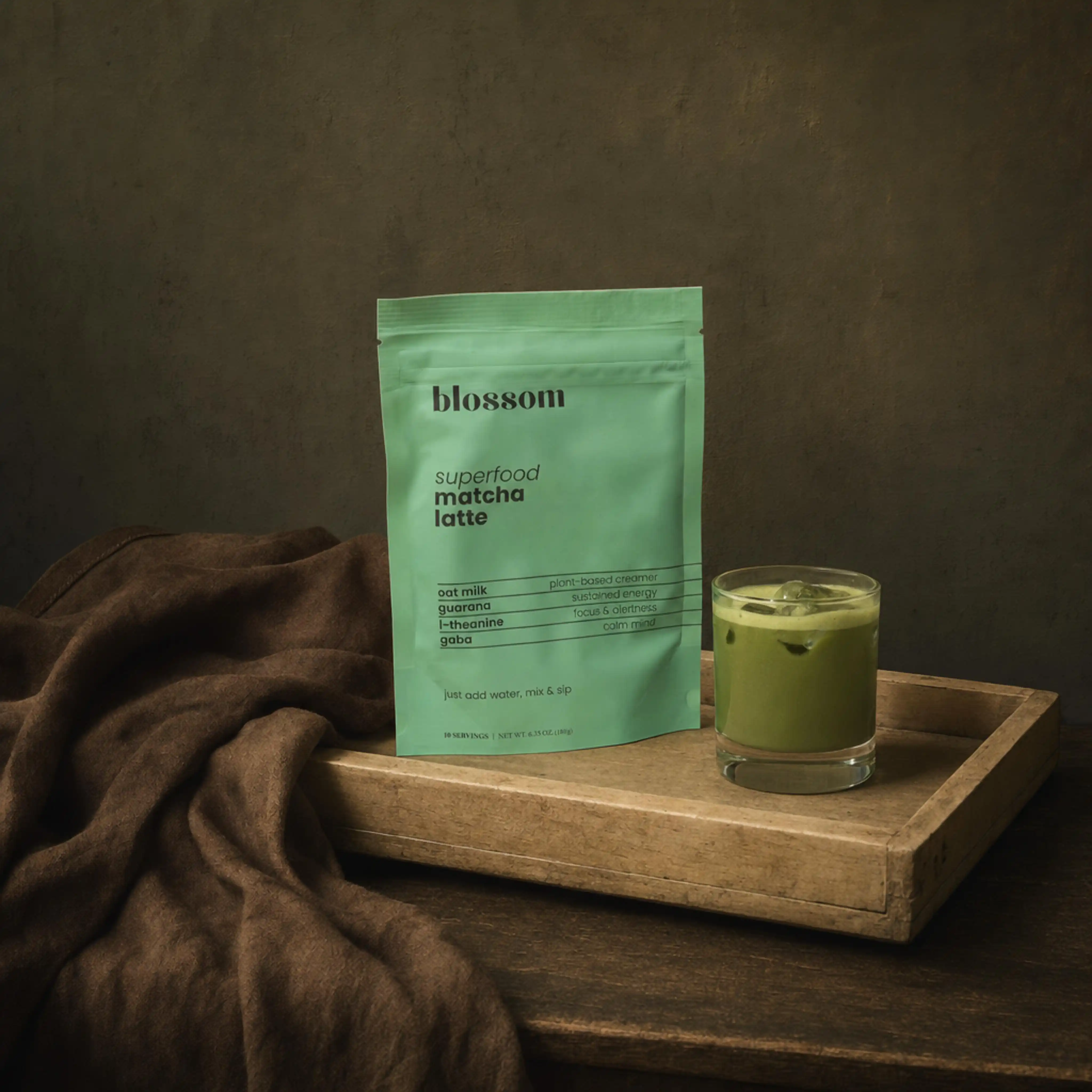 Green package of Blossom superfood matcha latte and a glass of iced matcha latte on wooden tray.