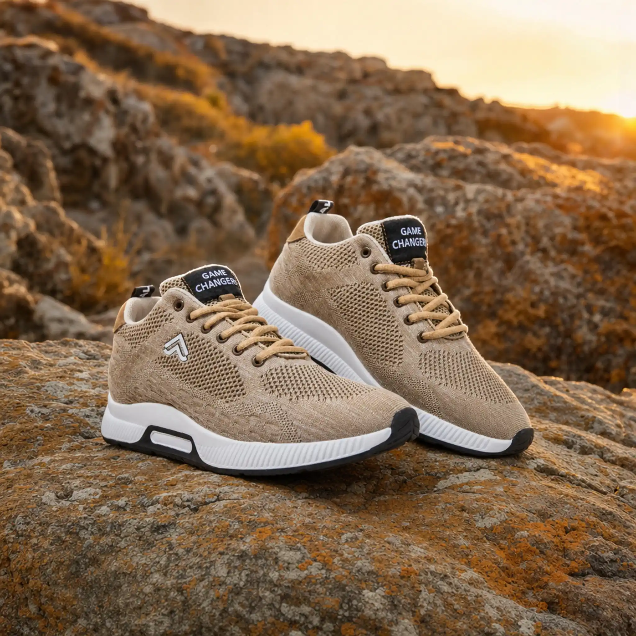 Pair of beige knit sneakers with white soles on rocky terrain at sunset.