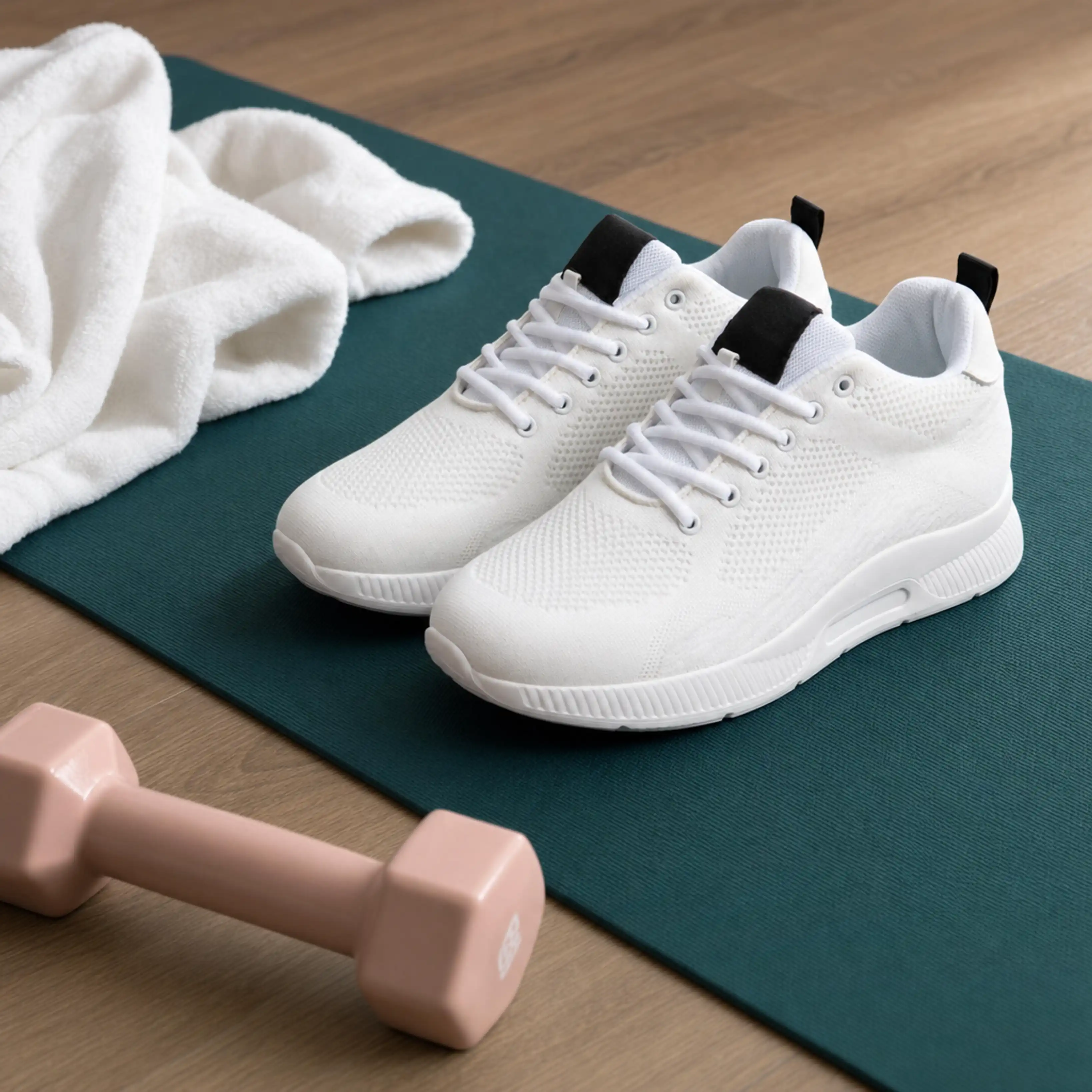 White athletic shoes on a teal mat next to a pink dumbbell and a white towel on wooden floor.