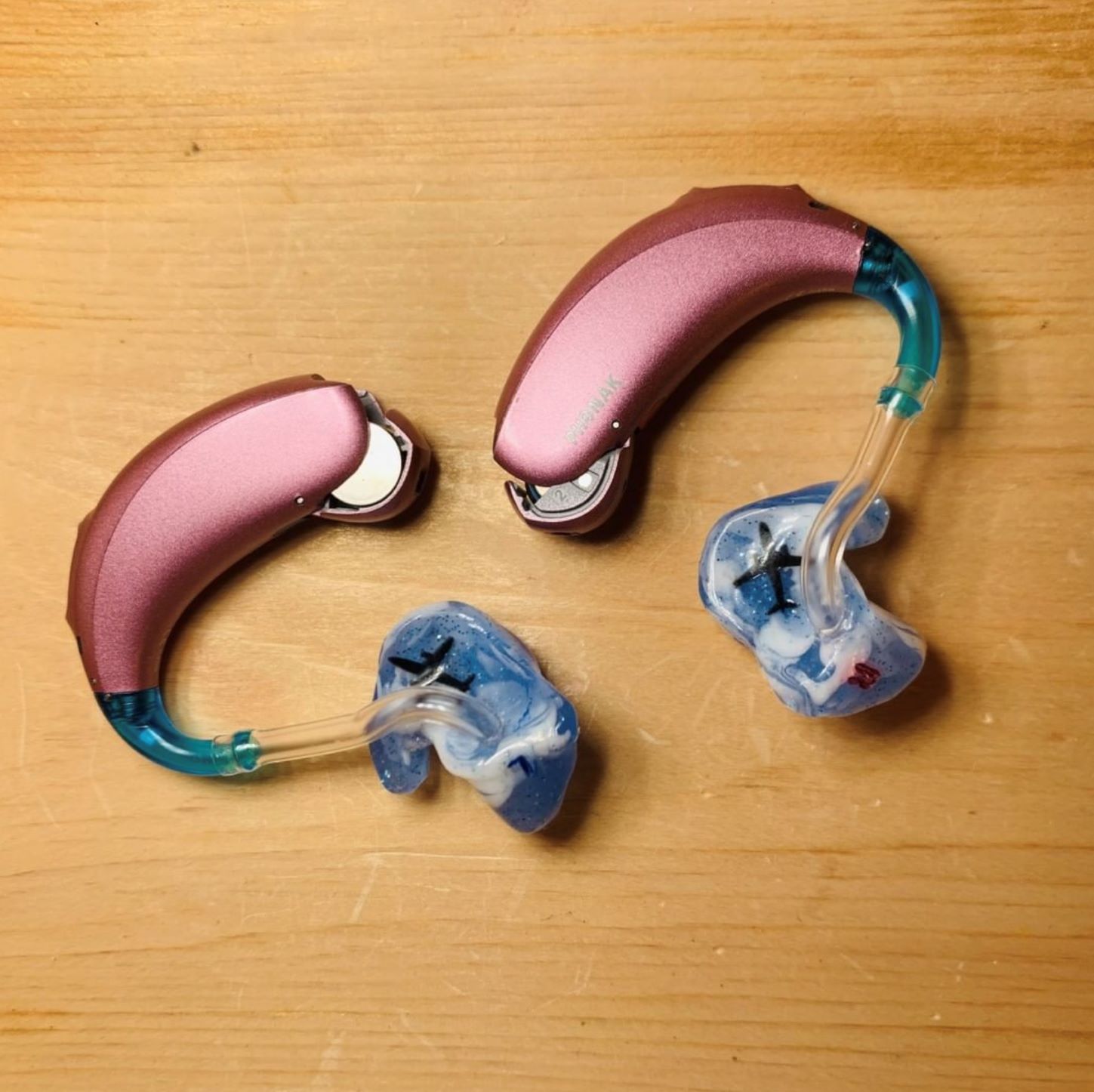 Pink Phonak pediatric hearing aids with blue and white earmolds