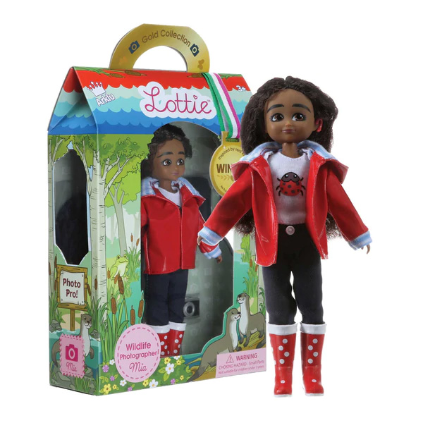 Lottie doll Mia wearing red cochlear implant, red boots and jacket, displayed next to product box