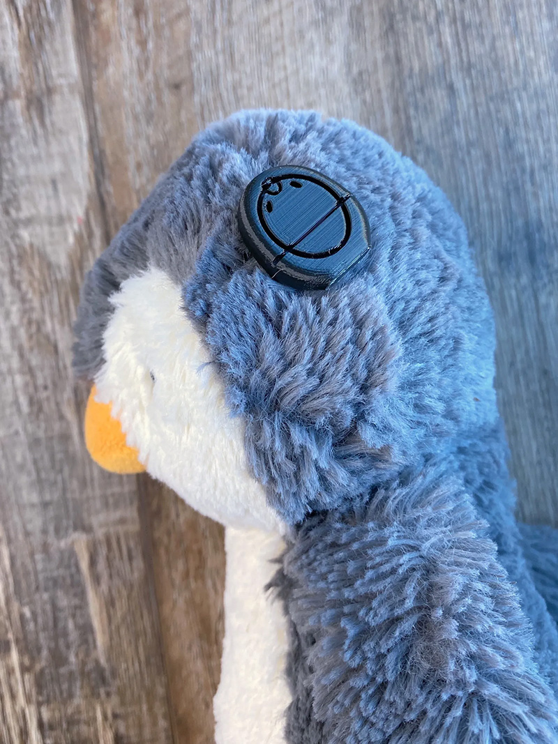 Grey and white stuffed penguin with yellow bill wearing cochlear implant, side view
