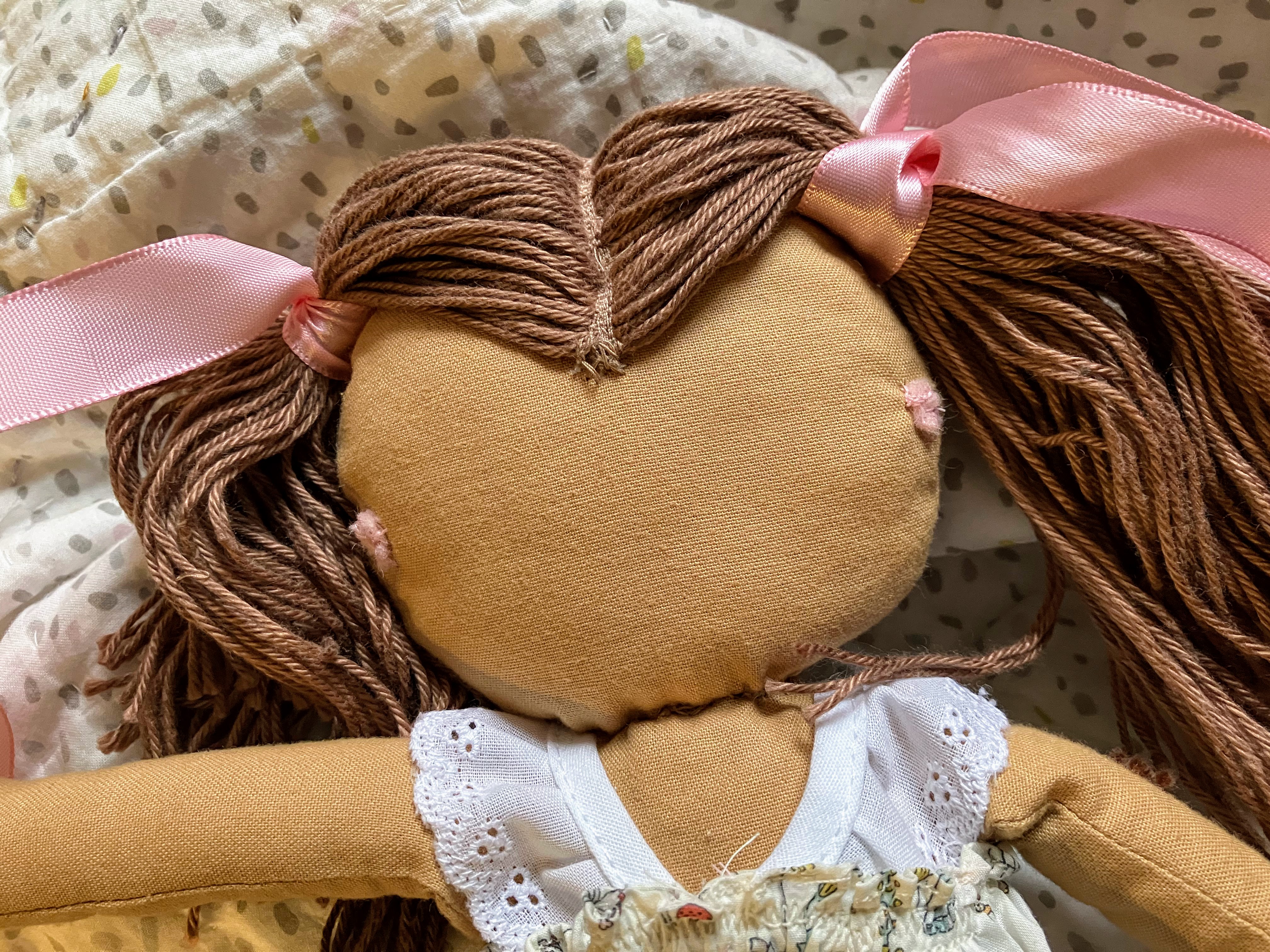 Doll head with two sewn-on felt hearing aids for DIY customization project matching child's own hearing devices for hard of hearing children