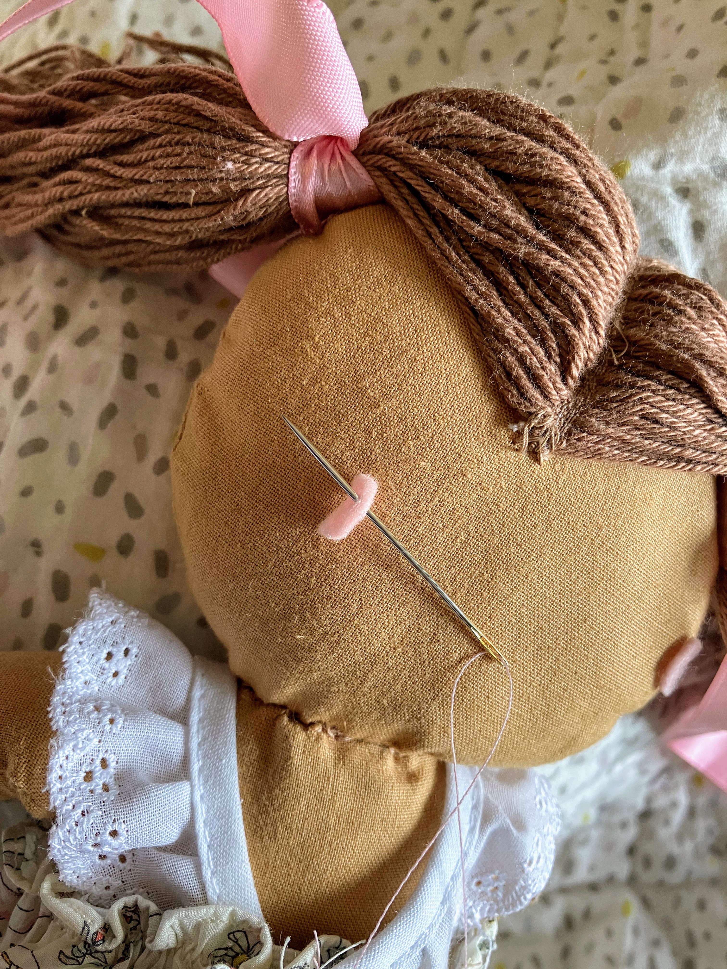 Close-up of hand sewing felt hearing aid onto doll head with needle and thread for DIY customization project for hard of hearing children