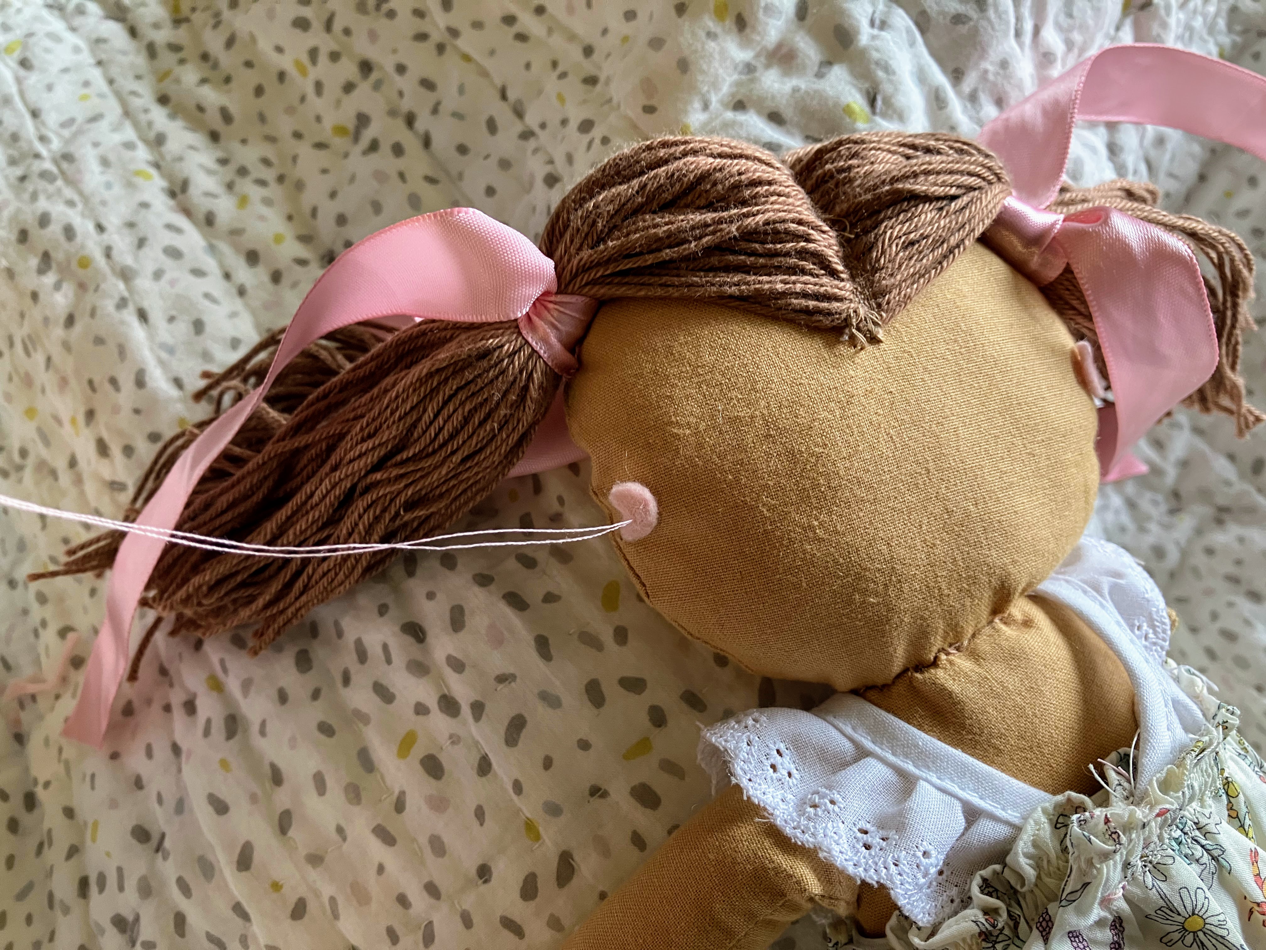 Photograph showing hand sewing felt hearing aid onto doll head with needle and thread for DIY customization project for hard of hearing children