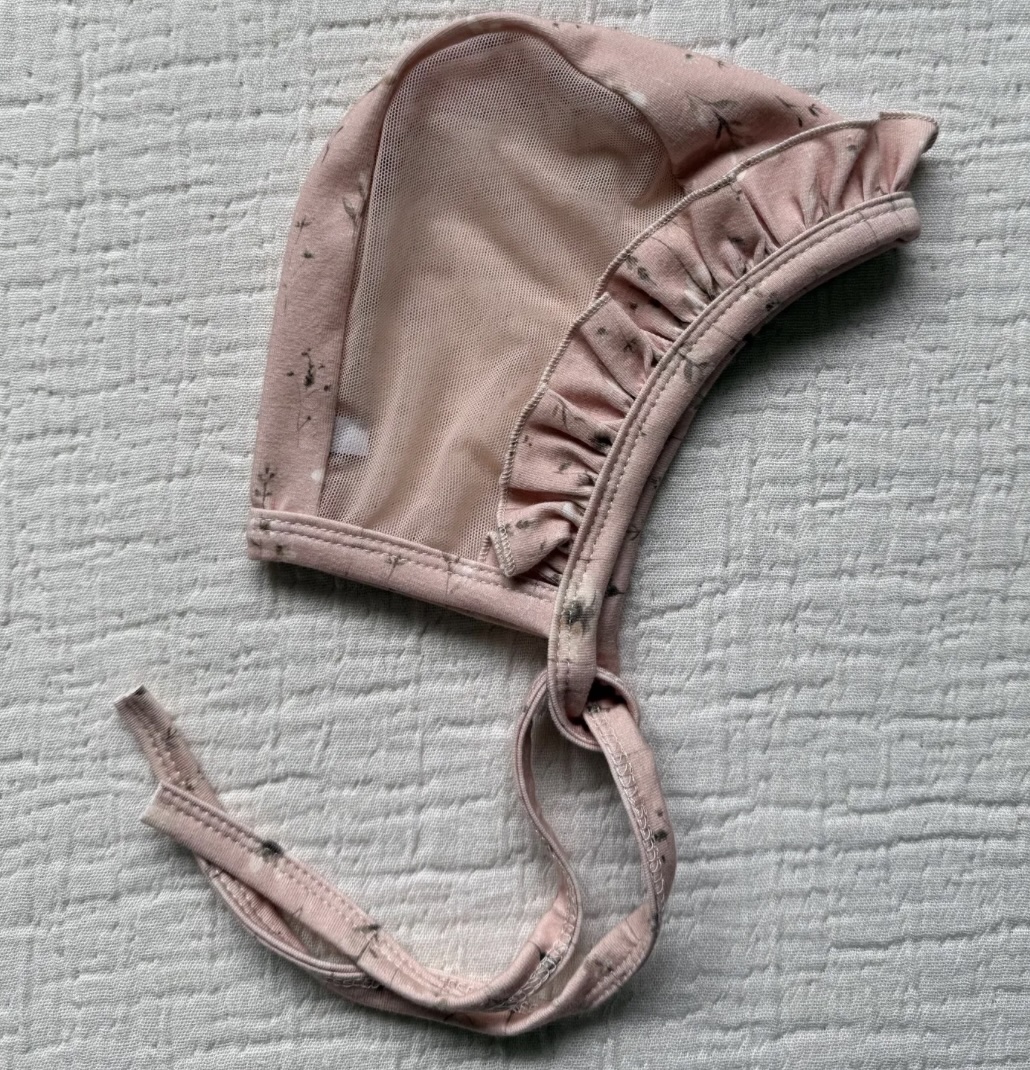 Emmifaye hearing aid bonnet with pink flower print, ruffle trim, and mesh lining, includes ties