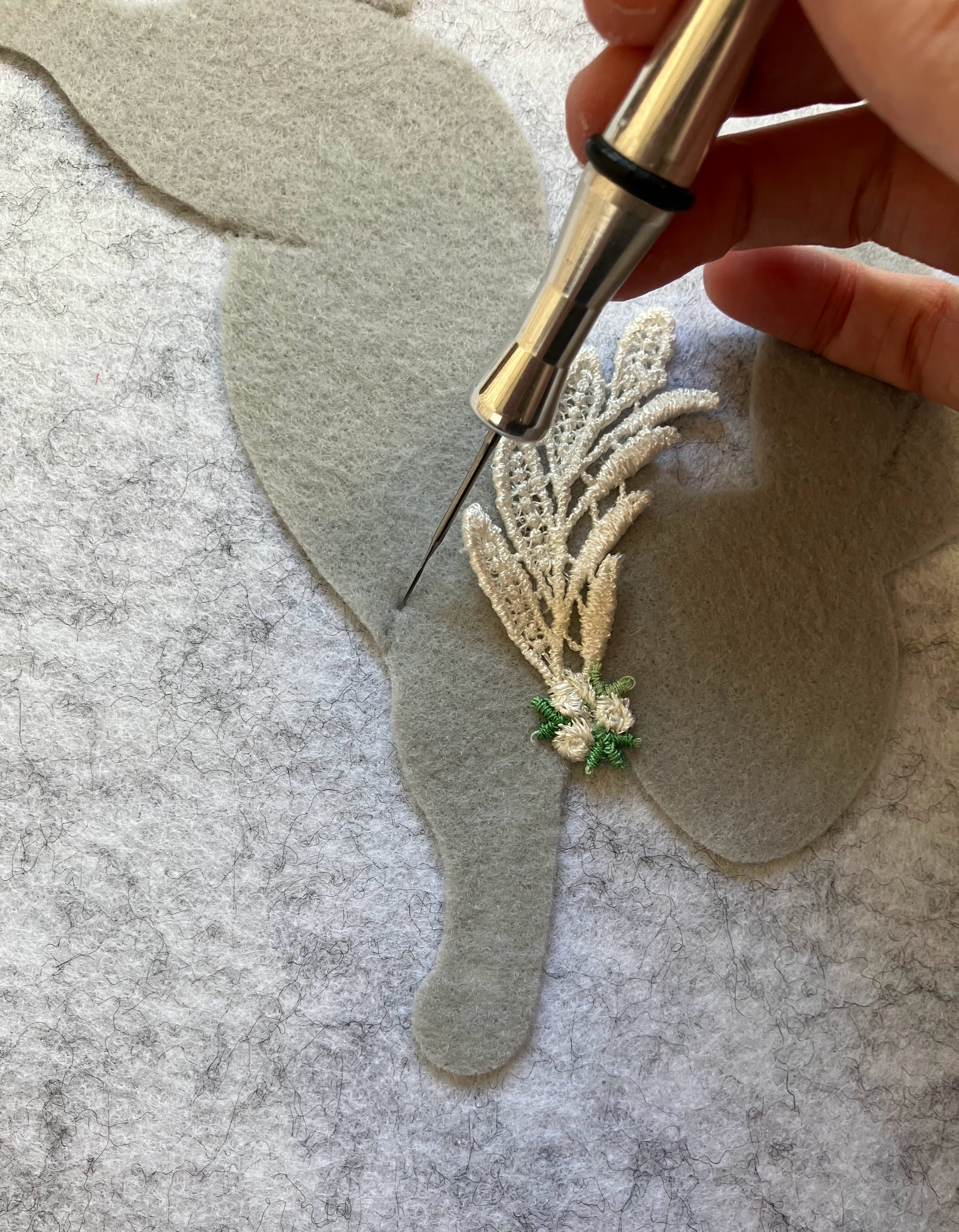Hand using needle felting tool to add embroidered botanical details to gray felt for acoustic panel decoration